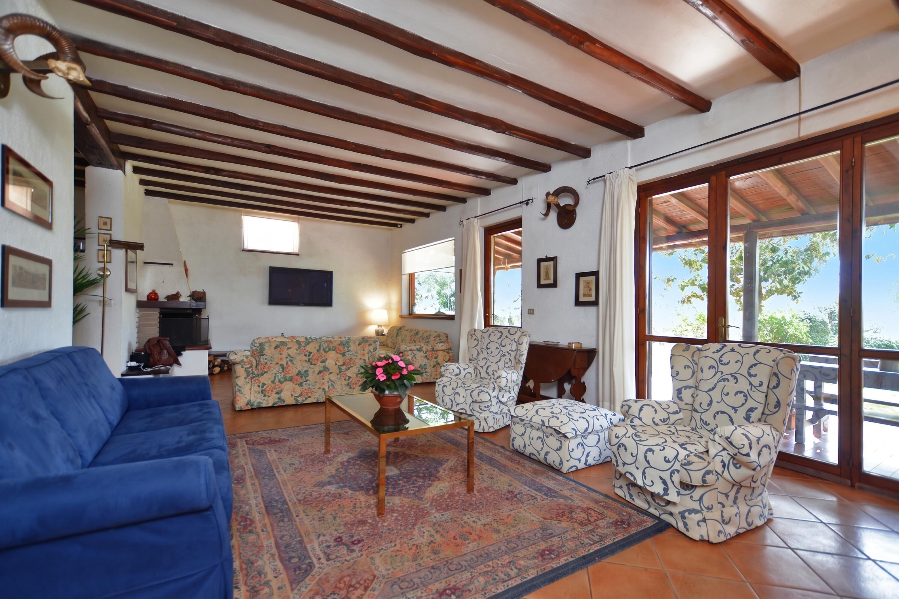 Una sala de estar con un sofá azul, sillones estampados, una mesa de centro con una planta y un ventanal con vistas.