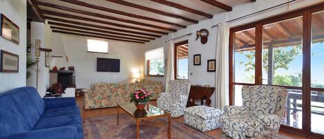 Una sala de estar con un sofá azul, sillones estampados, una mesa de centro con una planta y un ventanal con vistas.