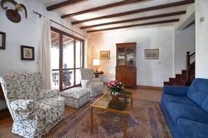 A living room with patterned armchairs, a blue sofa, a glass coffee table, and a cabinet. - Casale Pontarello (Vetralla)