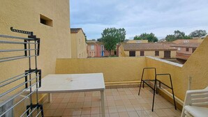 En balkon med et hvidt bord og stole, gelænder af metal og udsigt til omkringliggende bygninger.