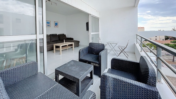 A balcony with wicker furniture, a sofa, and a table. - Air-conditioned apartment for 4 with pool, terrace and sea view (Le Barcarès)