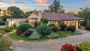 A two-story house with a red-tiled roof, surrounded by well-maintained gardens and a gravel driveway.