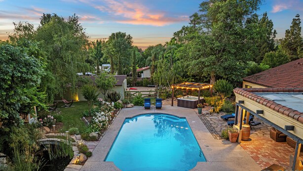 A backyard with a swimming pool, surrounded by a garden and trees.