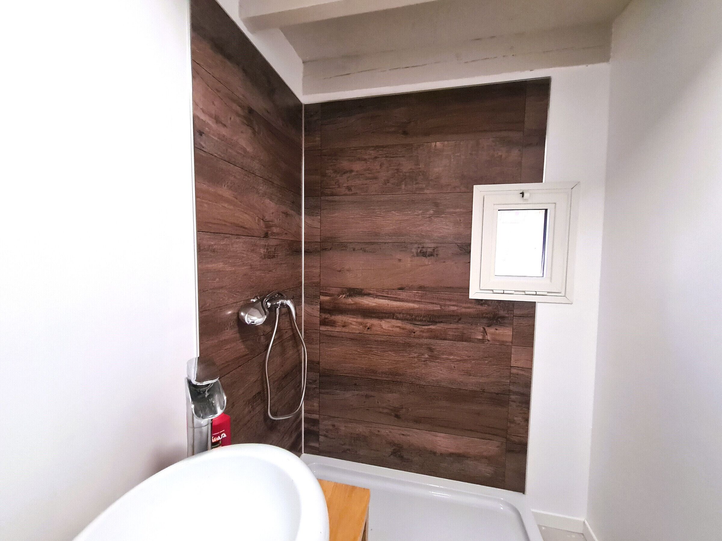 Une salle de bain avec un mur en bois, un lavabo blanc et une douche dotée d’un panneau de commande.