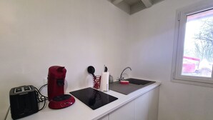 Een kleine kitchenette met een spoelbak, een rode koffiezetapparaat, een zwarte broodrooster en een zwart waterkoker.