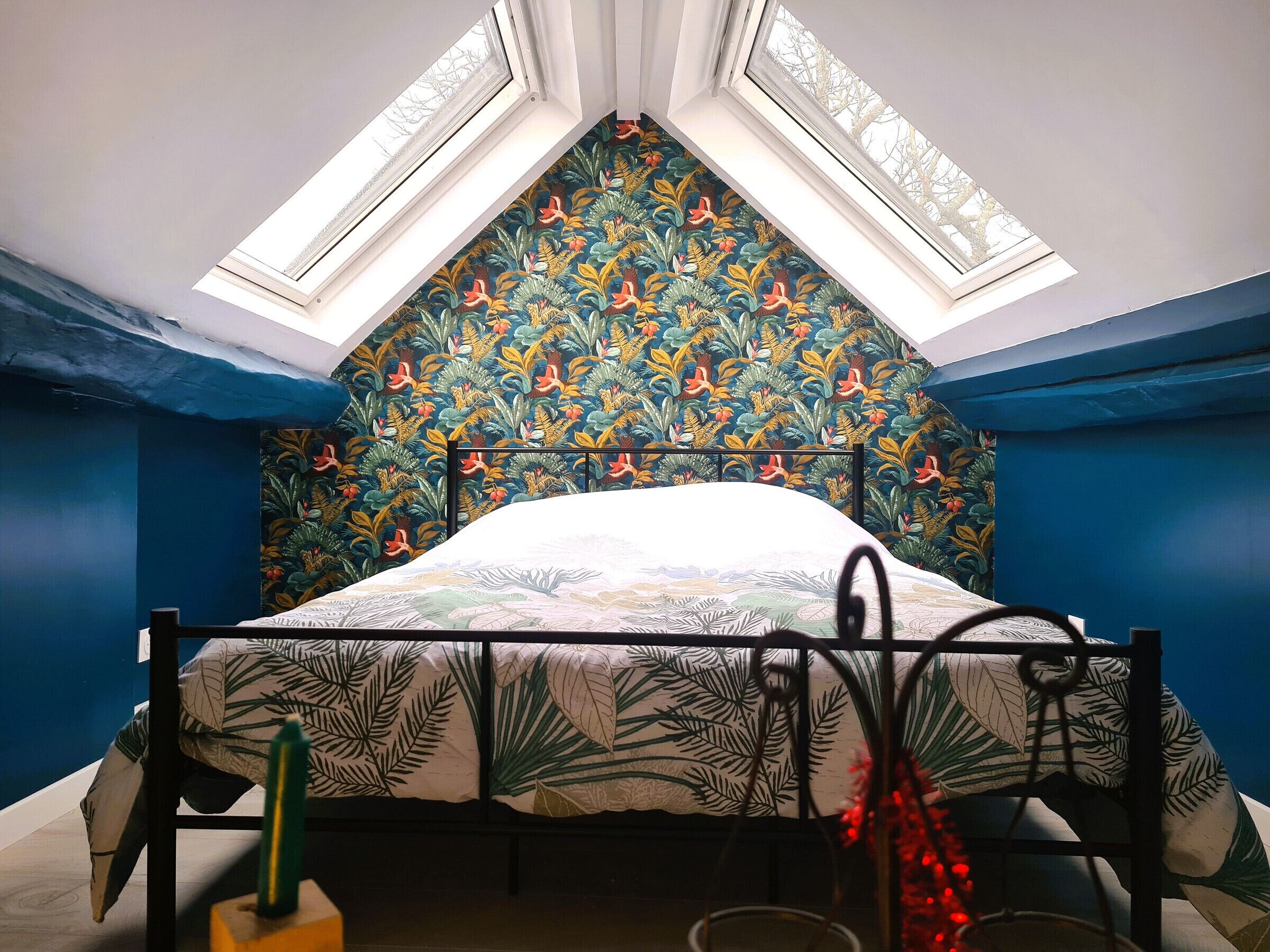 Ein Schlafzimmer mit schrägem Dach, einem Bett mit blumigem Kopfteil und einem Oberlicht.