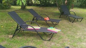Een rij comfortabele ligstoelen buiten, elk met een bijpassend tafeltje, op een gazon.