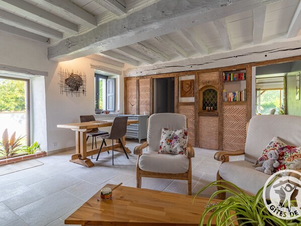 Un salon chaleureux avec une table à manger en bois, un canapé et un fauteuil. On y trouve une bibliothèque remplie de livres et un élément décoratif mural.