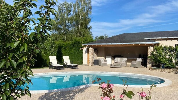 Una piscina con sillas de descanso, un porche cubierto y abundante vegetación.