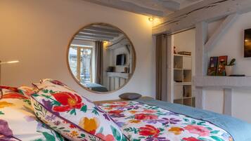 A bedroom with a bed, a round mirror, a bookshelf, and a window.