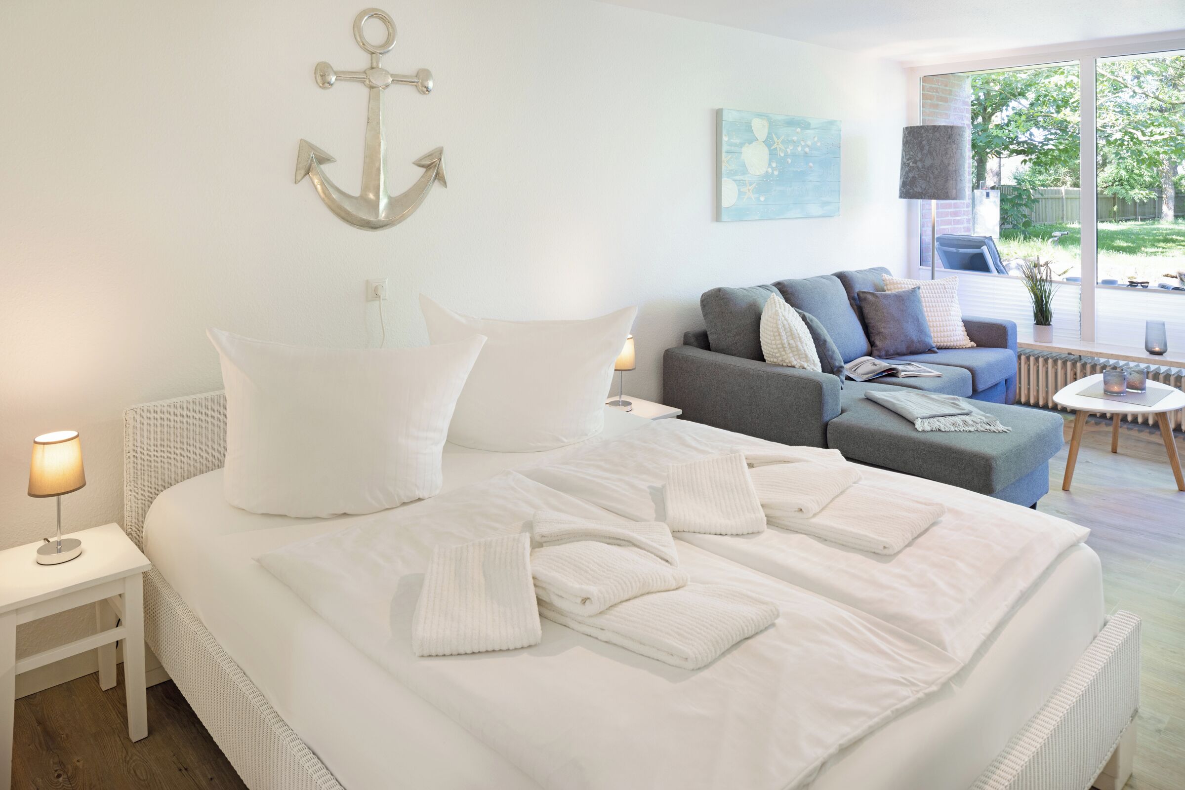 A bedroom with a bed, a nightstand, a sofa, and a view of the outdoors.