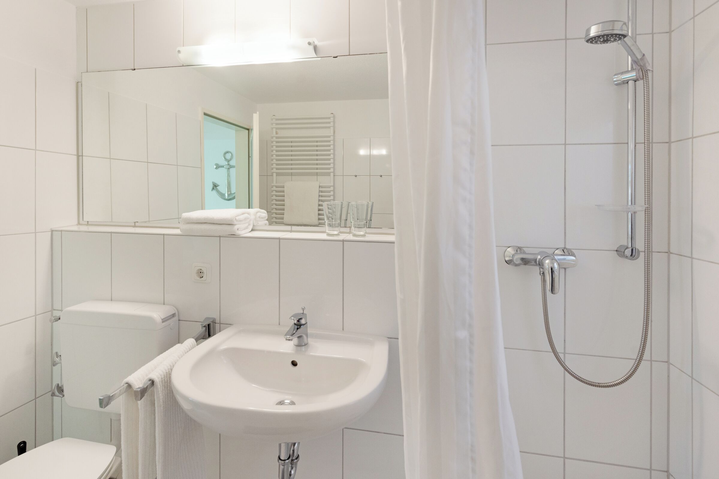Ein modernes Badezimmer mit Waschbecken, Toilette und Dusche, alles in Weiß.