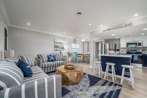 A modern living room with striped sofas, a wooden coffee table, and a kitchen area with bar stools.