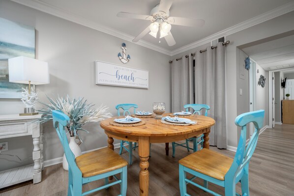 A dining area with a wooden round table, four turquoise chairs, a ceiling fan, and a wall-mounted sign.