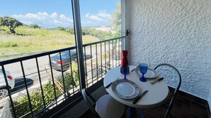 A balcony with a table set for two, overlooking a parking area and greenery.