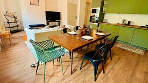 Un coin repas comprenant une table en bois, quatre chaises, un téléviseur et une cuisine avec des meubles de couleur verte.
