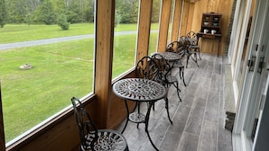 Un espace extérieur abrité, doté de murs en bois et de grandes fenêtres, aménagé avec des tables et des chaises en métal, ainsi qu’une cheminée en pierre.