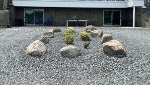 Un bâtiment à l’architecture moderne, doté d’une grande entrée vitrée et d’une allée gravillonnée agrémentée de gros rochers et de petits arbustes.