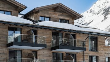 A wooden chalet with multiple balconies, large windows, and a snowy mountain backdrop.