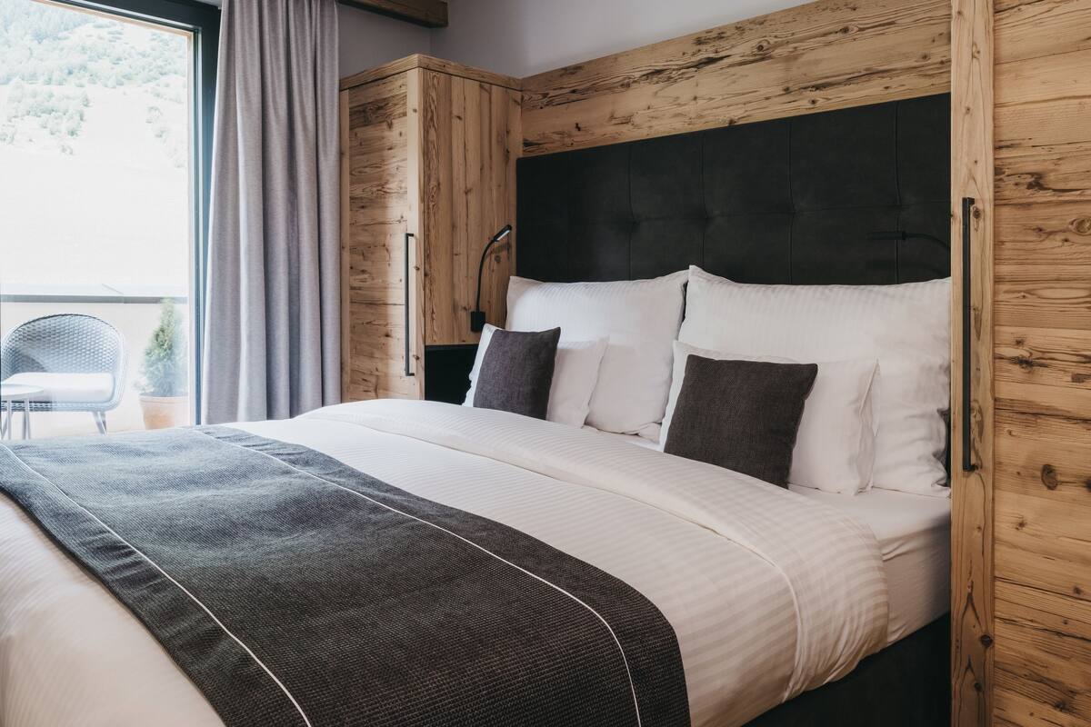 Une chambre moderne avec un grand lit, un lambris en bois et une vue sur un paysage enneigé par la fenêtre.
