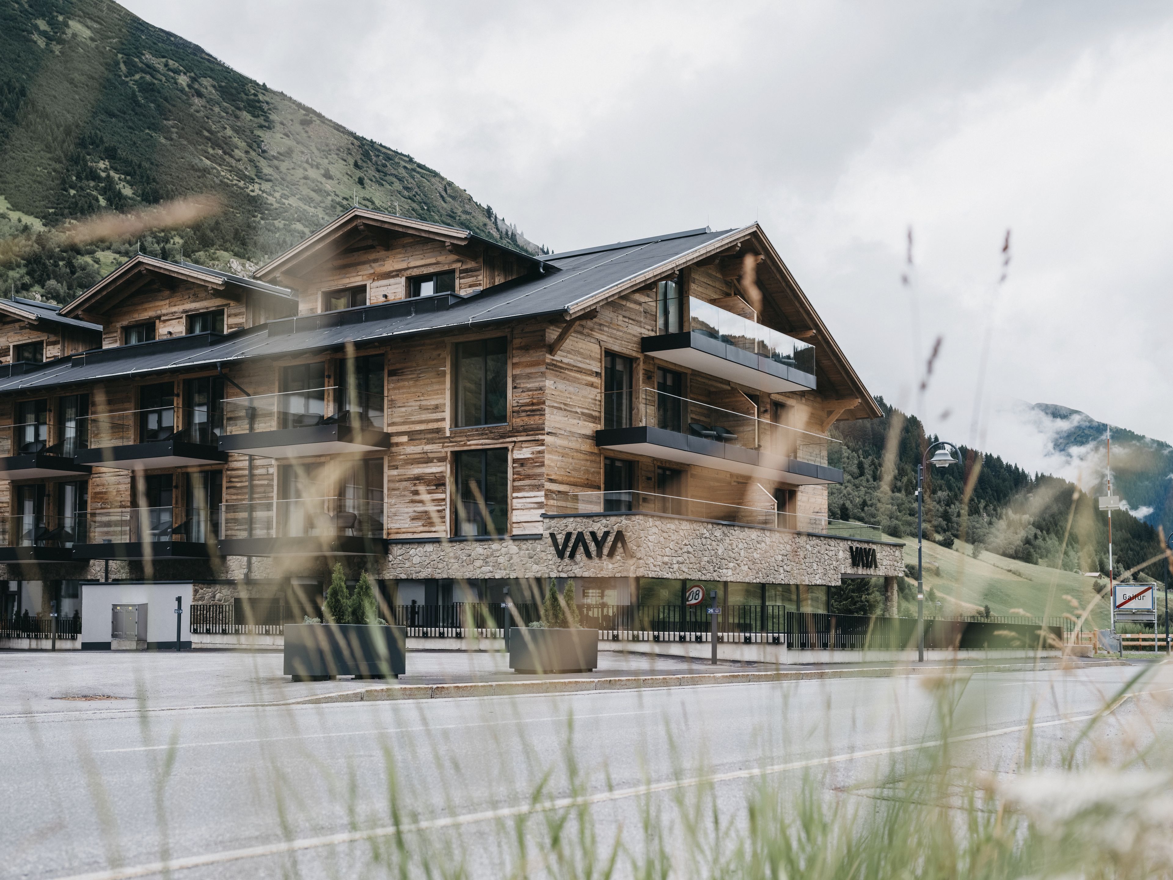 Un edificio de madera de varios pisos con balcones, una base de piedra y el nombre 'VAYA' a la vista.
