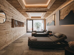 A spa room with a wooden wall, a massage table, and a large window. - VAYA Residence Galtür (Galtür)