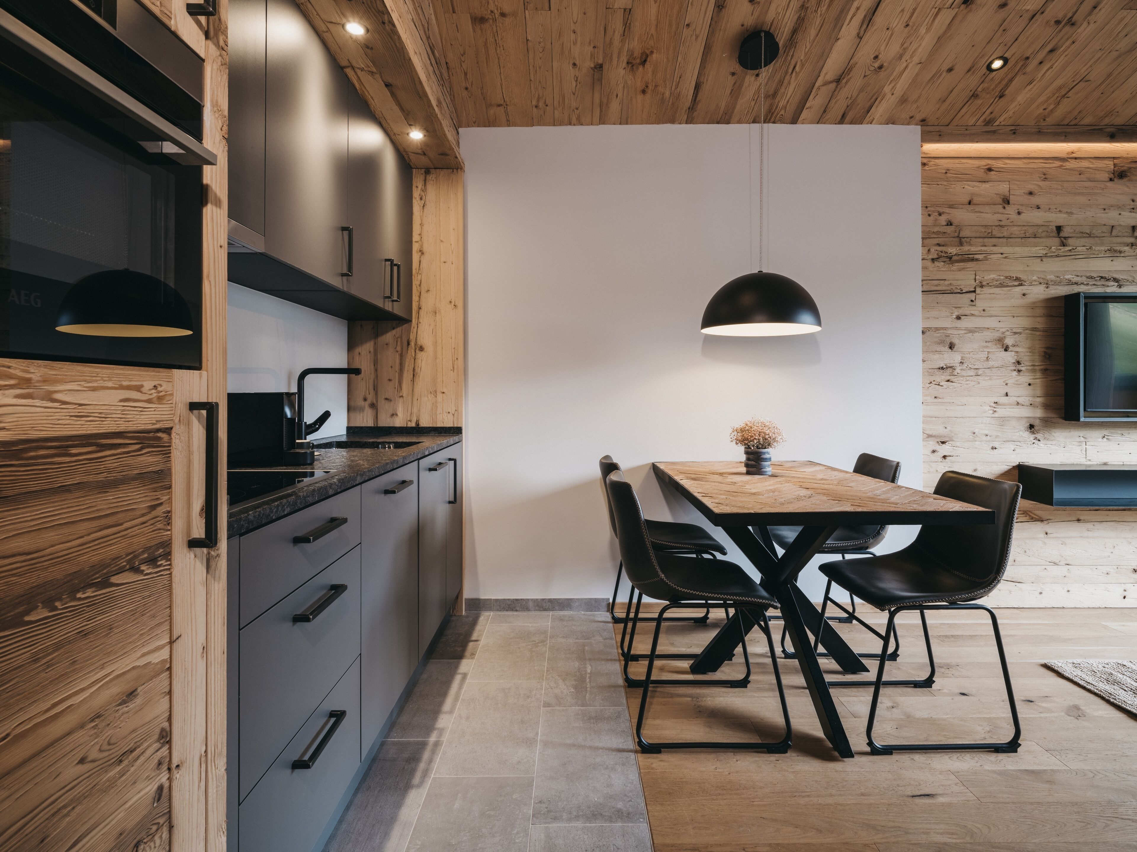 Une cuisine moderne avec des meubles en bois, un coin repas avec une table et des chaises en bois, et un téléviseur fixé au mur.