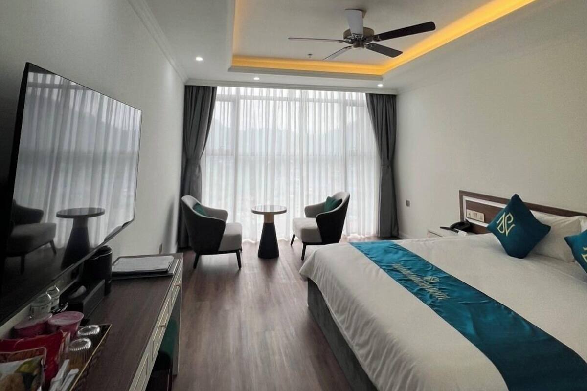 Una habitación de hotel moderna con una cama, dos sillones, una mesita, un televisor y un ventilador de techo.