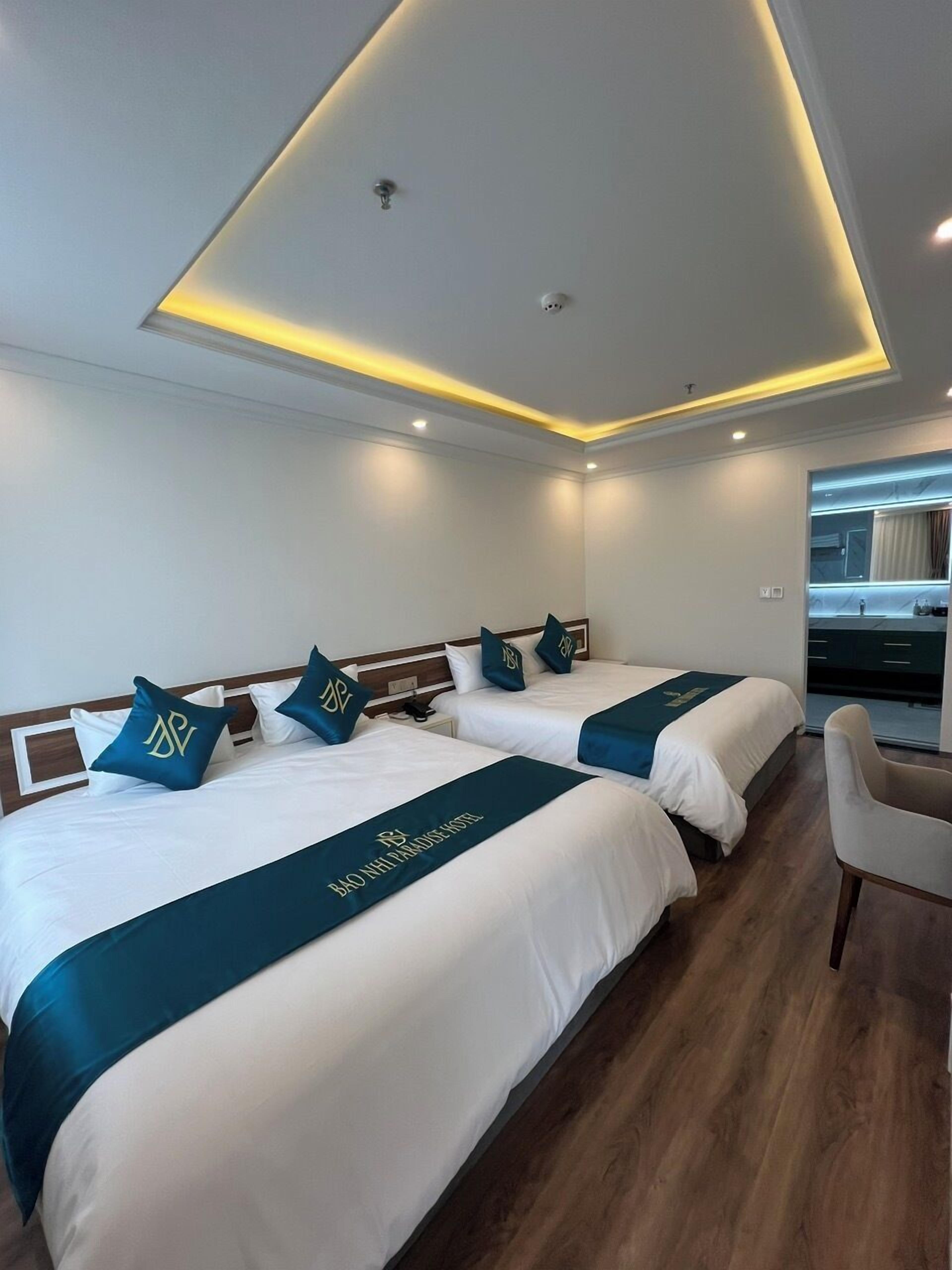 Habitación de hotel con dos camas, cada una con cabecera y almohadas a juego, y un escritorio con silla.