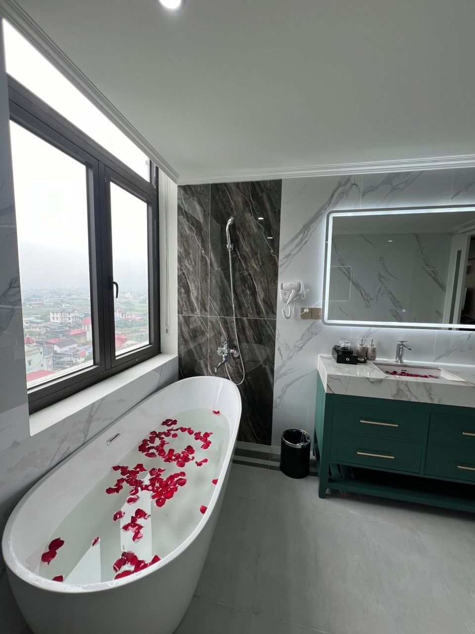 A modern bathroom with a freestanding bathtub, a large mirror, and a view of the city through a window.
