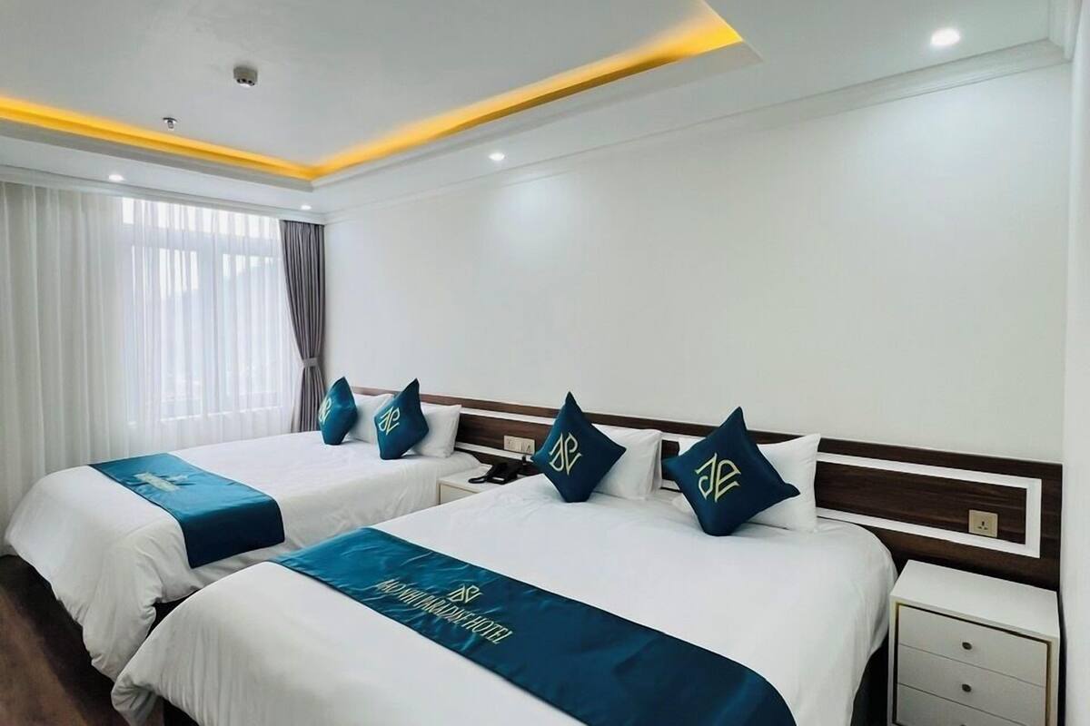 Habitación de hotel con dos camas, cada una con cabecera azul y almohadas a juego. El piso es de madera, las paredes son blancas y el techo tiene iluminación empotrada.