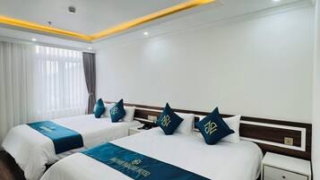 Habitación de hotel con dos camas, cada una con cabecera azul y almohadas a juego. El piso es de madera, las paredes son blancas y el techo tiene iluminación empotrada.