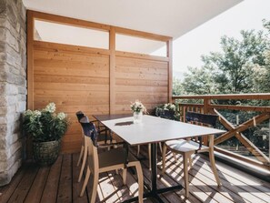 A wooden deck with a table and chairs, a potted plant, and a view of trees. - Village Park Suites (Zell am See)