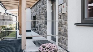 A modern building with a stone exterior, a wooden pergola, and a metal door. - Village Park Suites (Zell am See)
