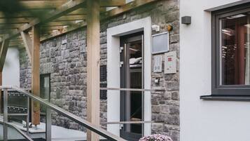 A wooden staircase leading to a stone wall entrance with a door, a window, and a small potted plant.