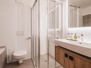 Une salle de bain moderne avec une douche à parois de verre, des toilettes blanches et un meuble-lavabo en bois avec un miroir.