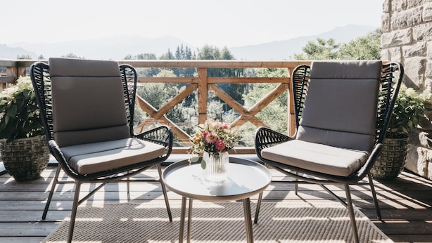 A wooden deck with two cushioned chairs and a small table with a vase of flowers. - Village Park Suites (Zell am See)