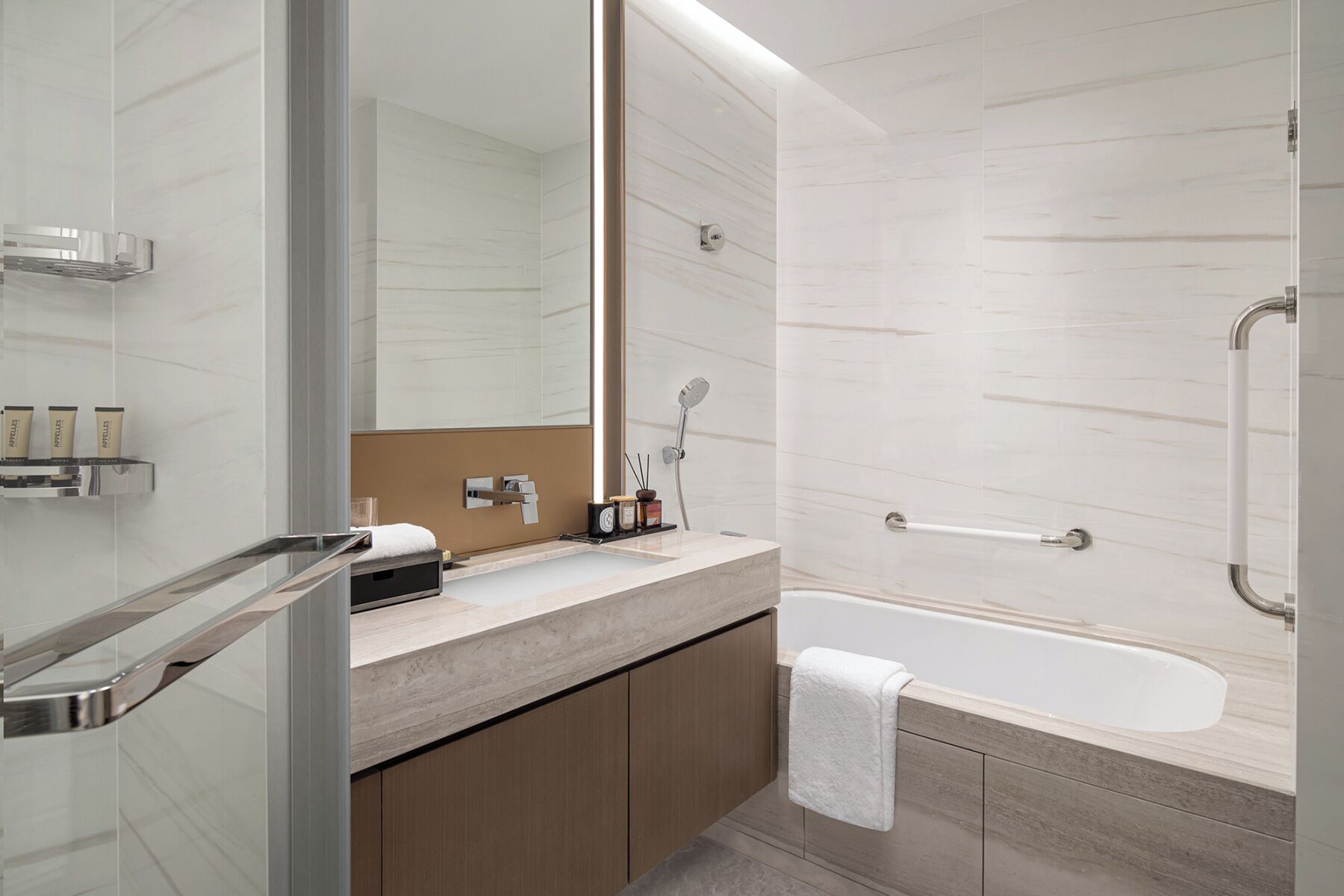 A modern bathroom with a bathtub, a large mirror, and a vanity with toiletries.