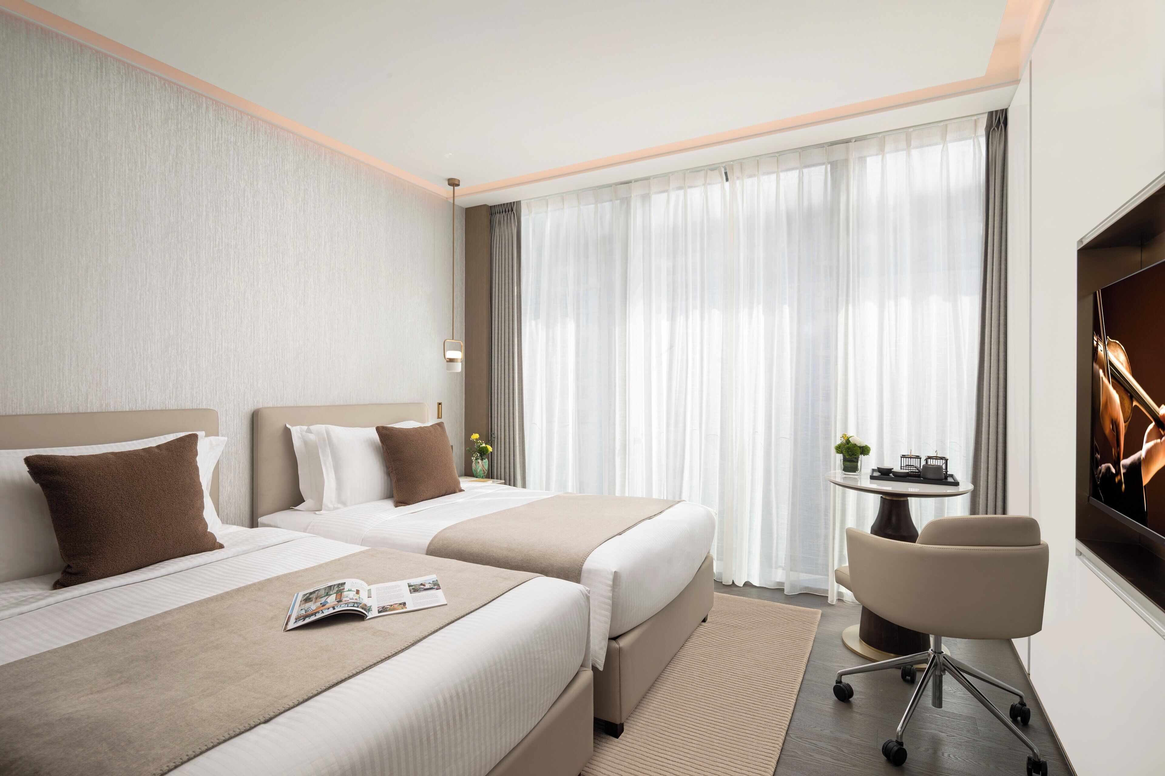 A hotel room with two beds, a desk, and a TV.