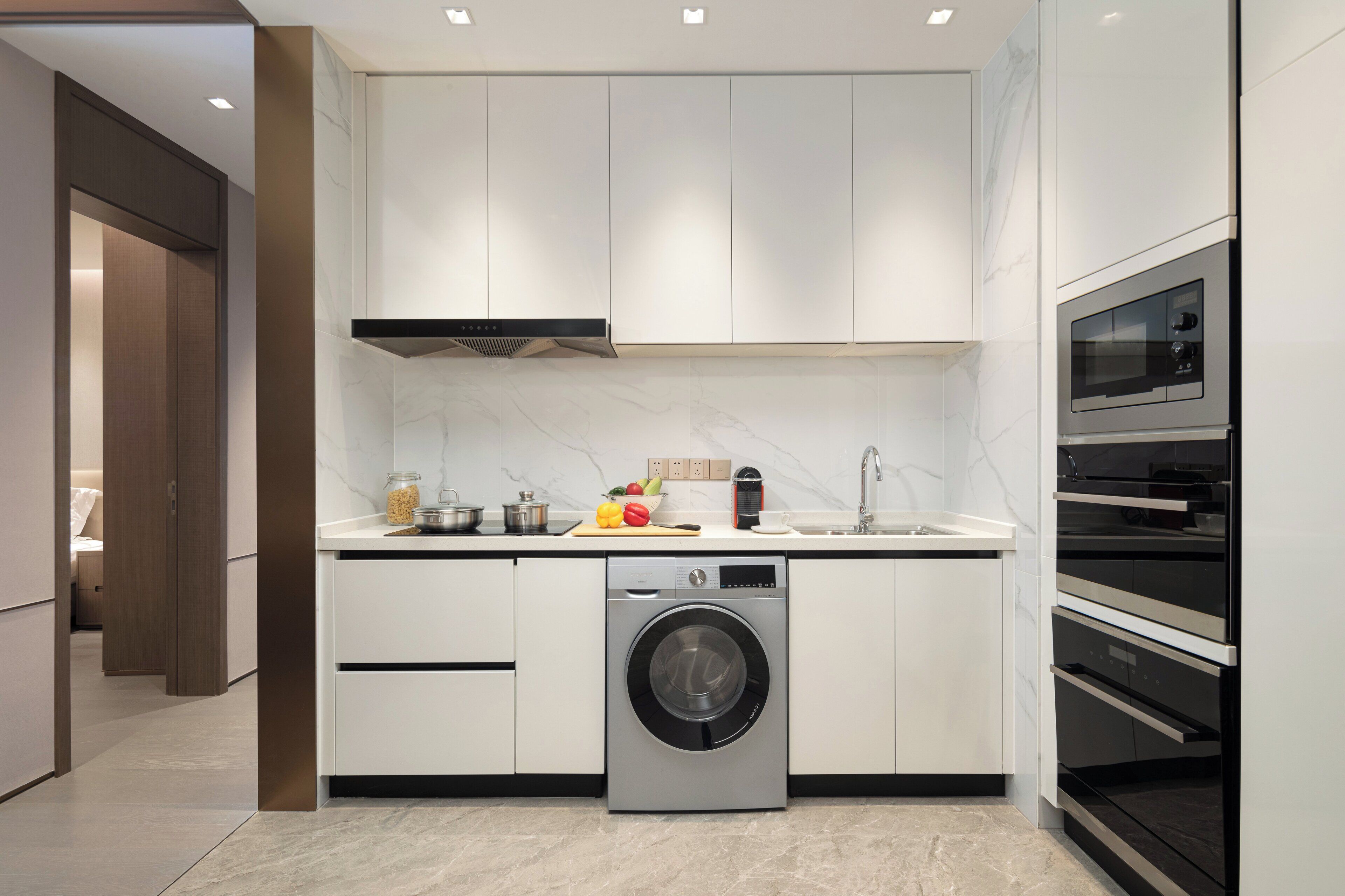 A modern kitchen with a built-in washer and oven, marble countertops, and a wooden cabinet.