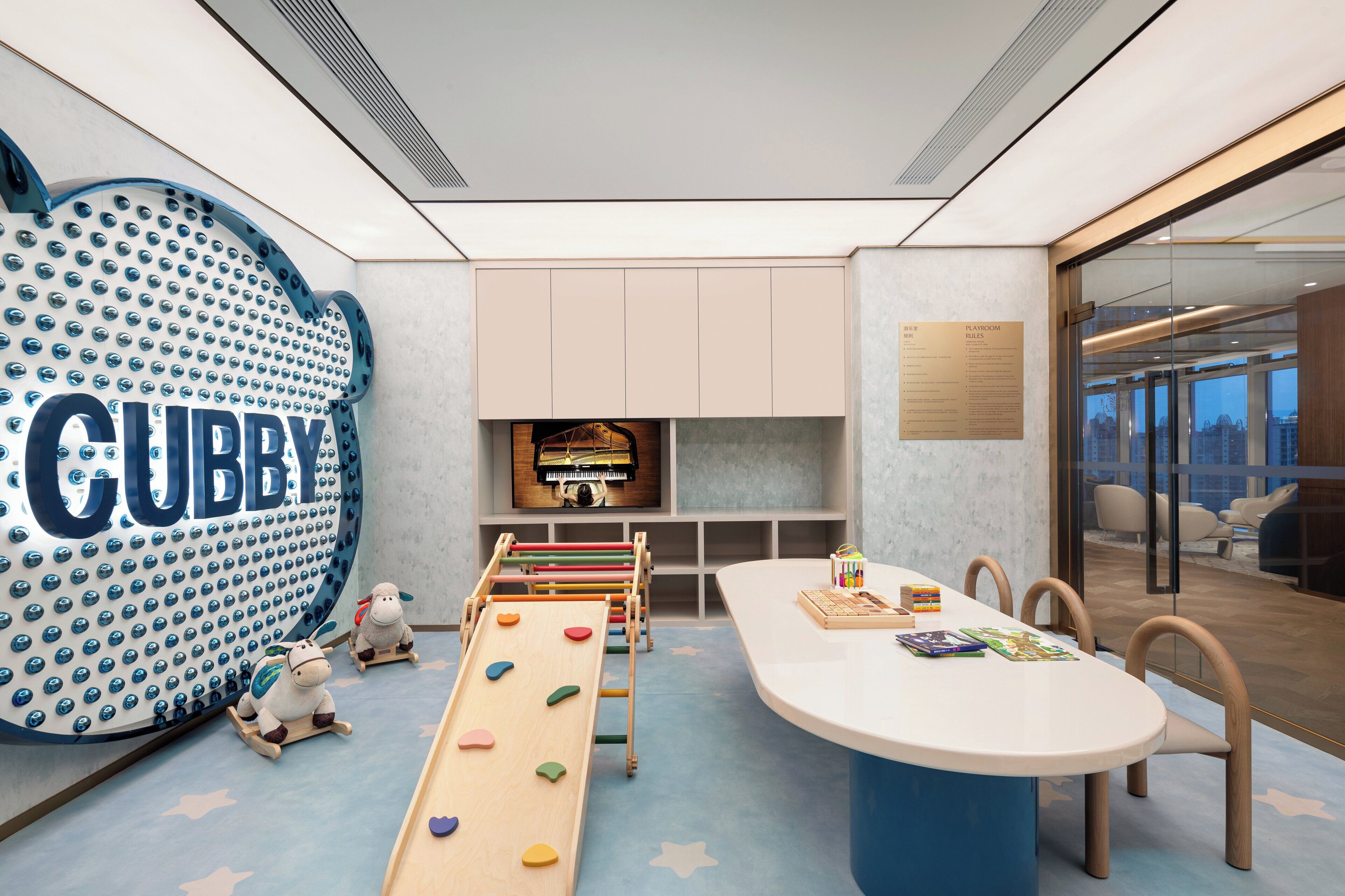 Un espace de jeux moderne pour enfants, avec un grand panneau indiquant « CUBBY », un mur d’escalade et une table de jeux avec des chaises.