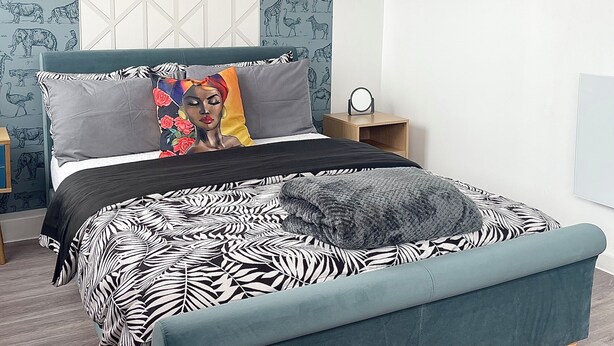 A bedroom with a bed, a nightstand, a window, and a wall with animal prints.