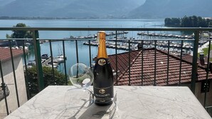 Une bouteille de vin Franciacorta et un verre sur un balcon donnant sur une marina, avec des bateaux et des montagnes en arrière-plan.