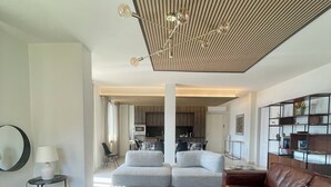 Un salon moderne avec un canapé d’angle, un divan en cuir marron, une table basse et, au fond, un coin repas.