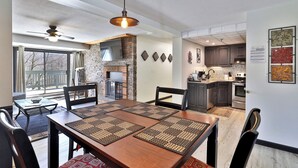Un comedor con mesa y sillas de madera, chimenea y cocina al fondo.