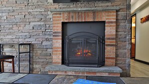 Una chimenea con marco de piedra y una reja metálica, una mesa con sillas y un libro en el suelo.