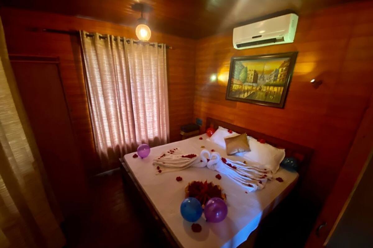 Ein Hotelzimmer mit Holzboden, einem Bett mit weißer Bettwäsche, einem Bild an der Wand und einer Klimaanlage.