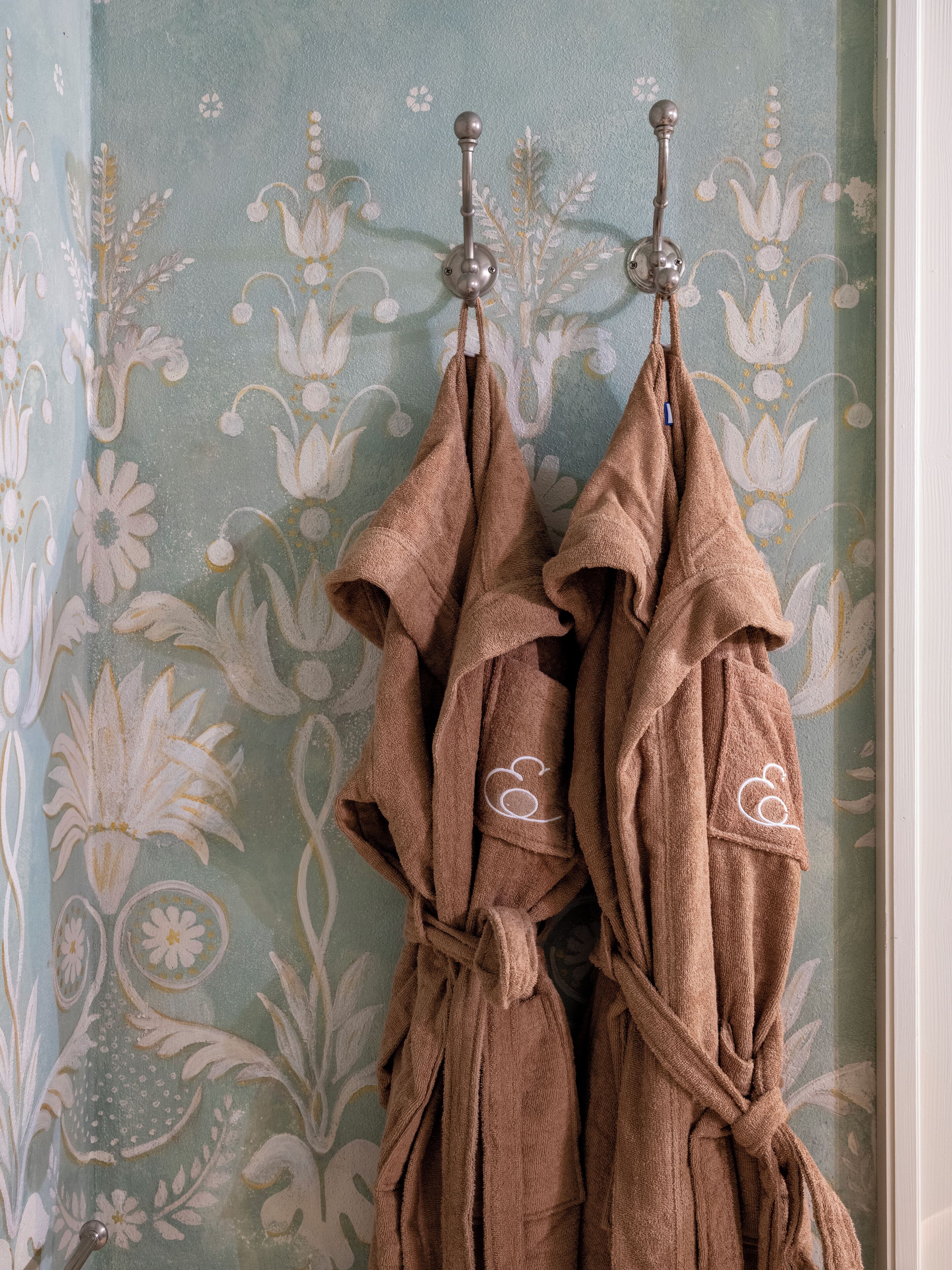 Un baño con papel tapiz floral, dos toallas colgadas en un perchero, y un perchero visible.