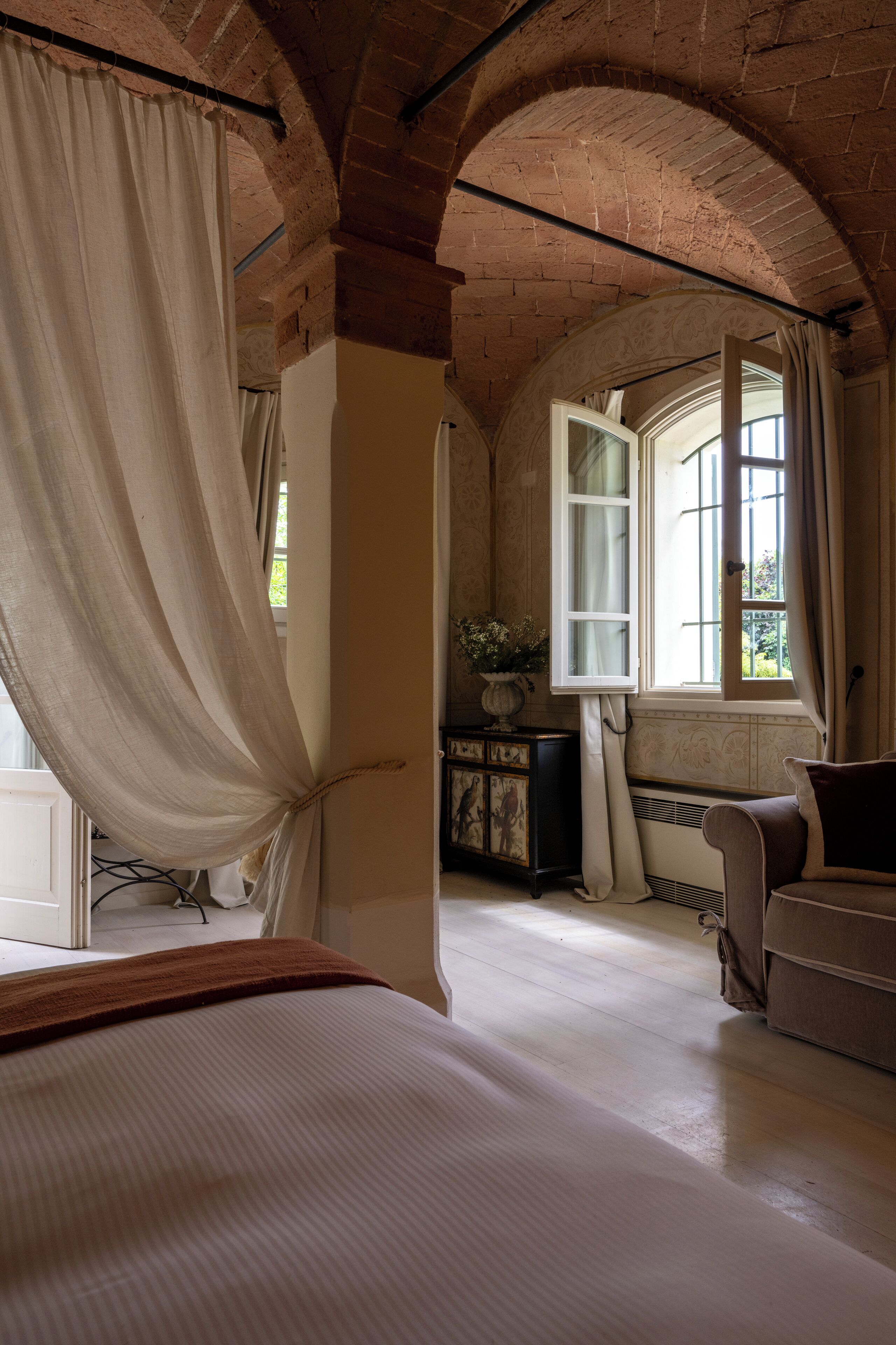 Una habitación con cama, sofá, ventana con cortinas y techo de ladrillo.