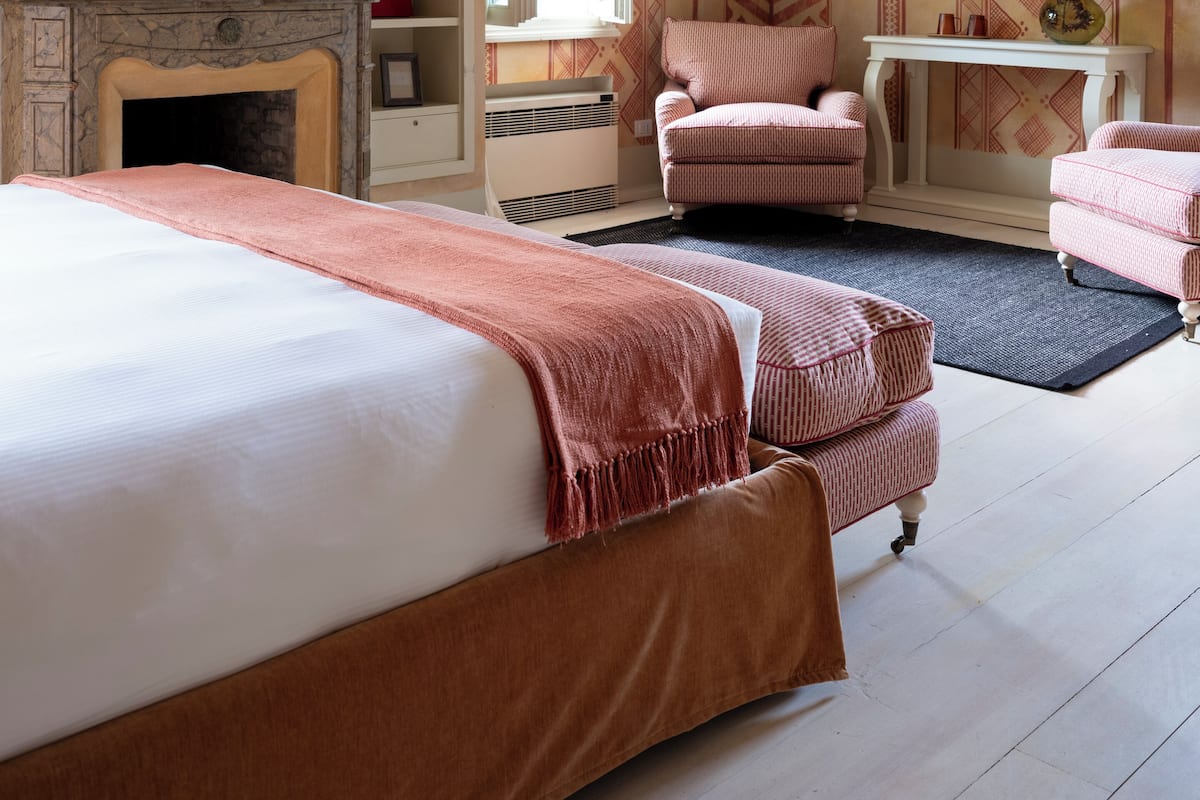 A bedroom with a large bed, a chair, a desk, and a fireplace.